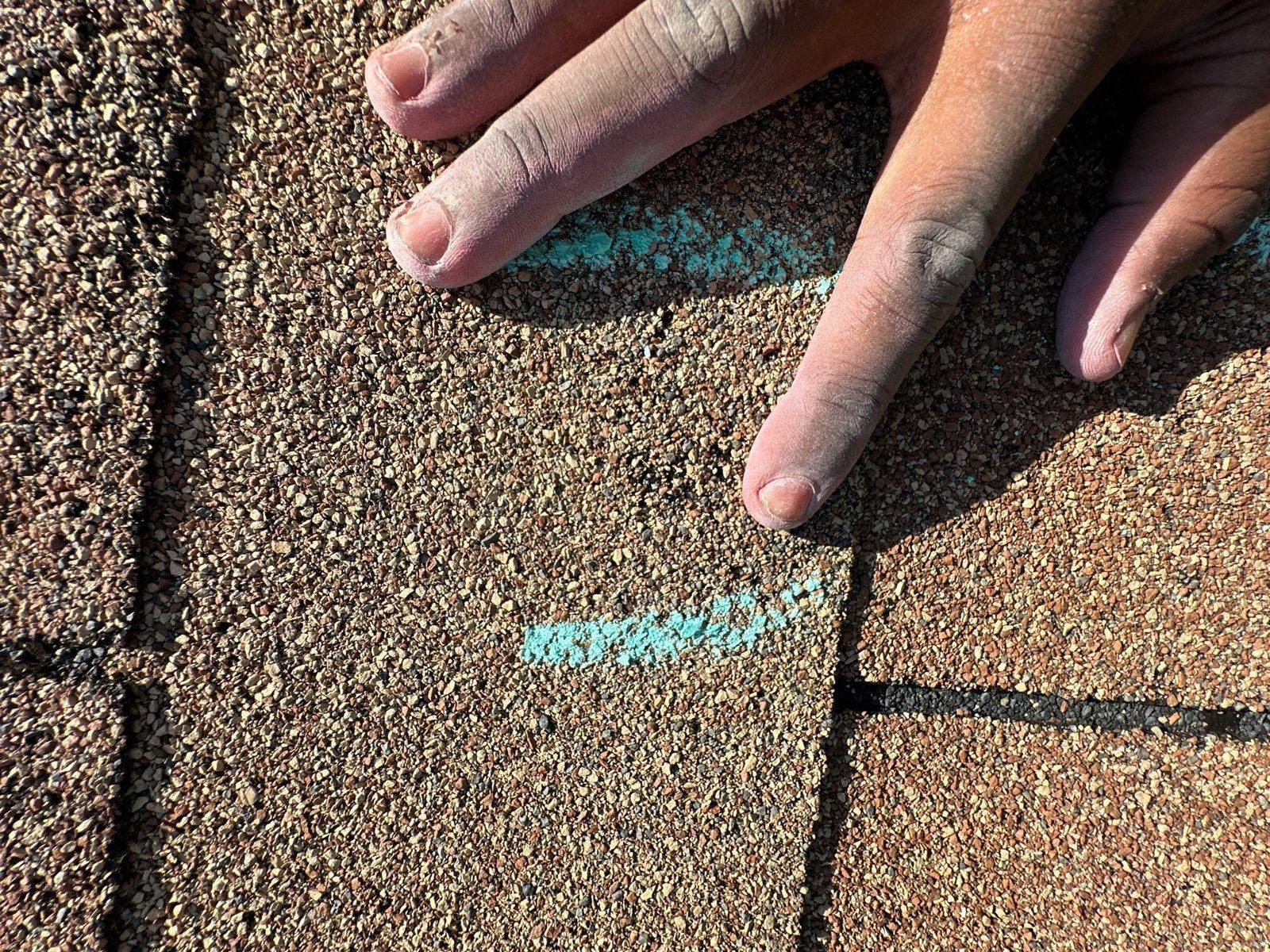 Two turquoise chalk marks on a brown shingle with a hand beside them for scale