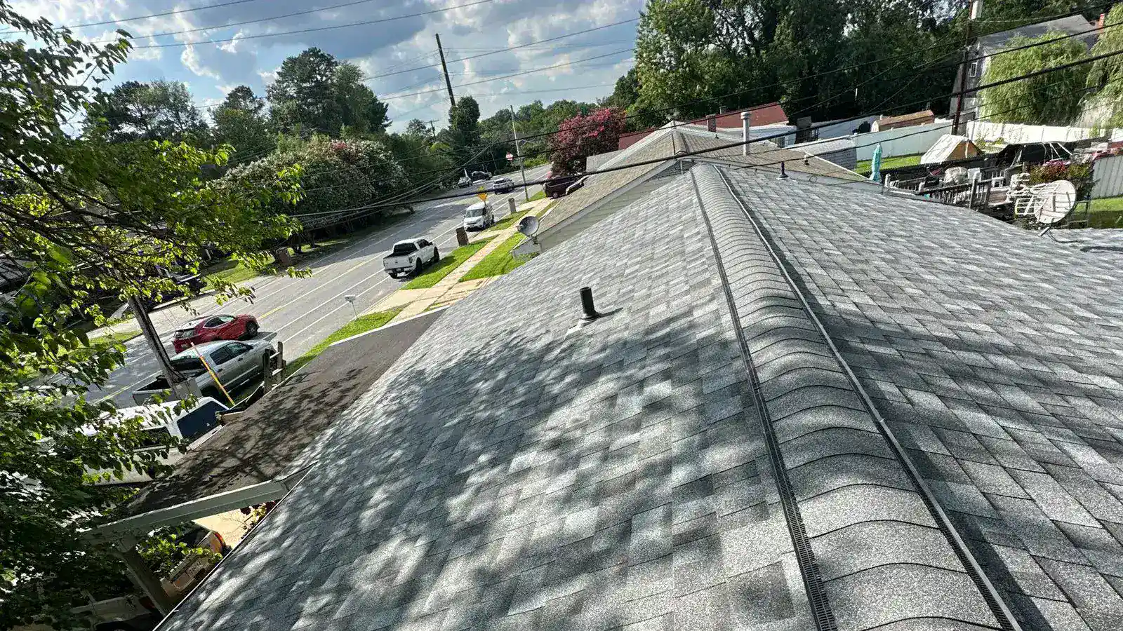 Light gray shingle roof with a ridge vent and ridge cap up the centre, dappled tree shade across the slope