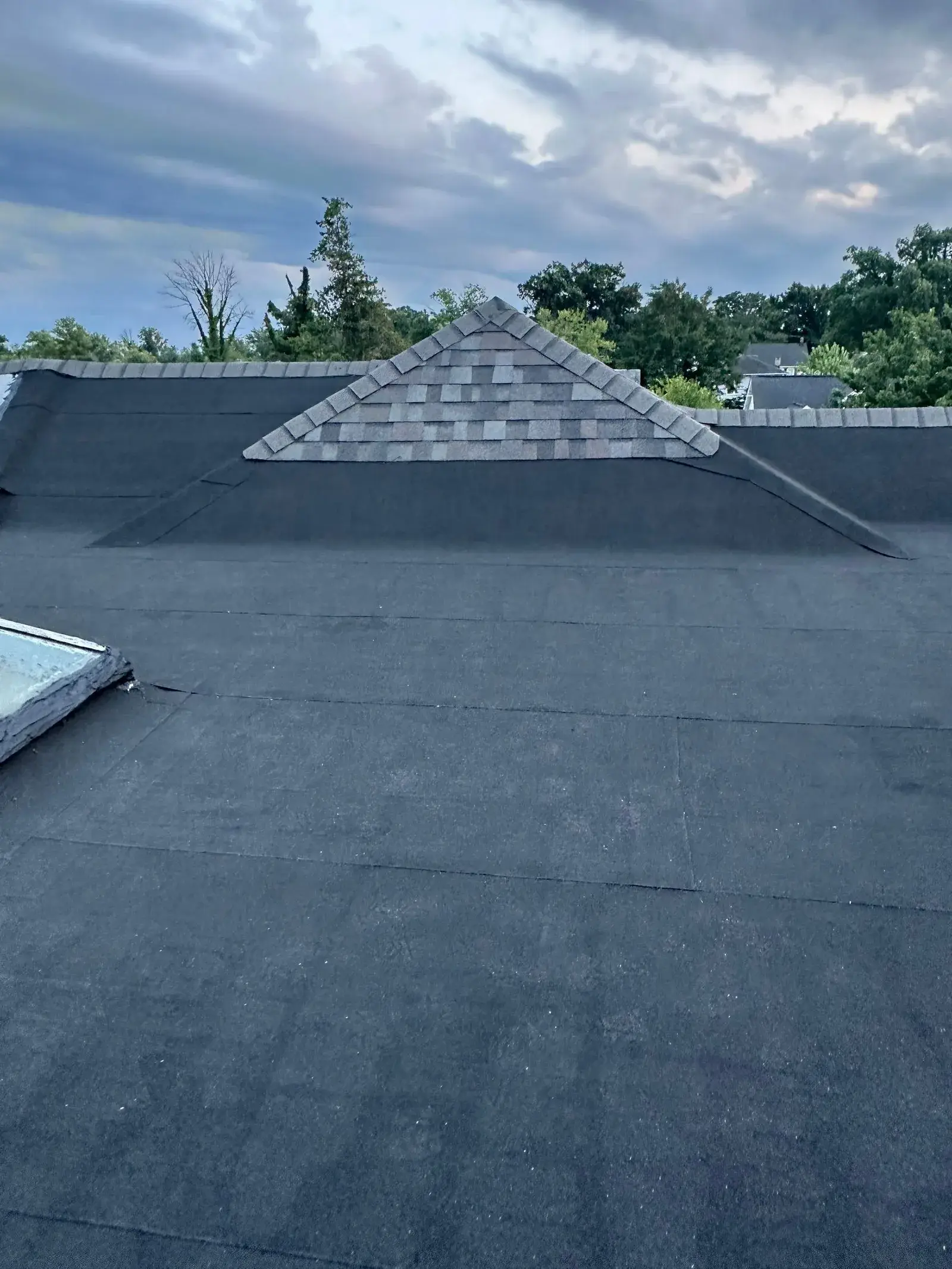 Finished low-slope roof in smooth black modified bitumen, with a shingled gable dormer and shingled caps on the parapet